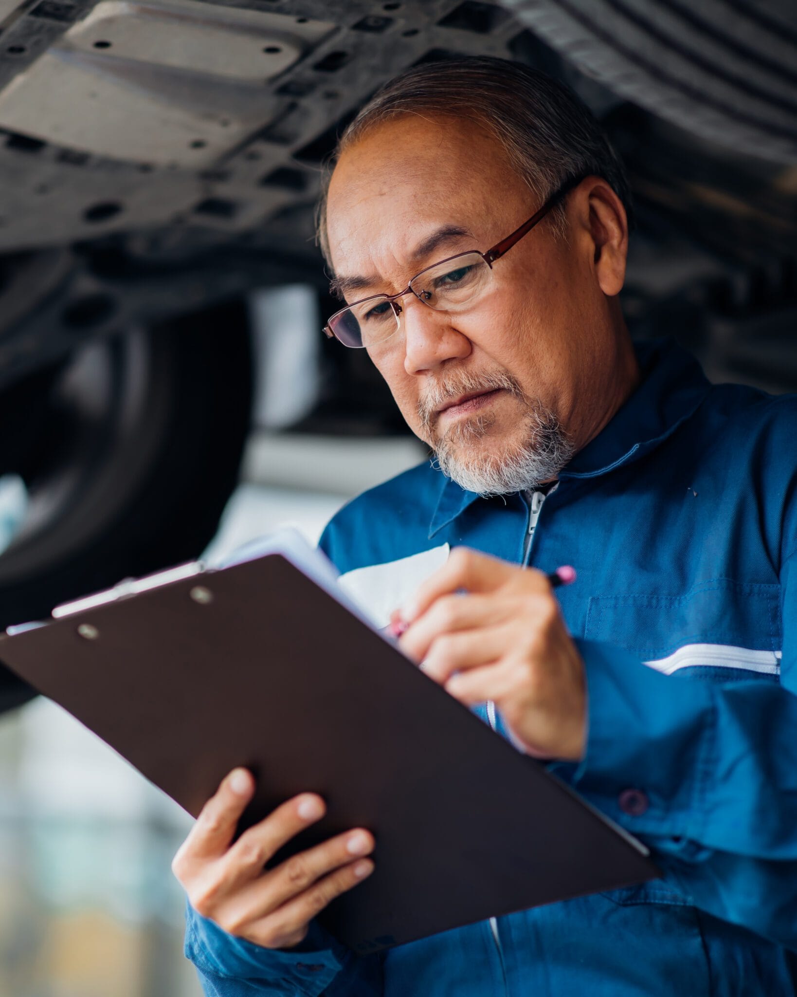 Asian Senior man mechanic working Under a Vehicle in a Car Service station. Expertise mechanic working in automobile repair garage.